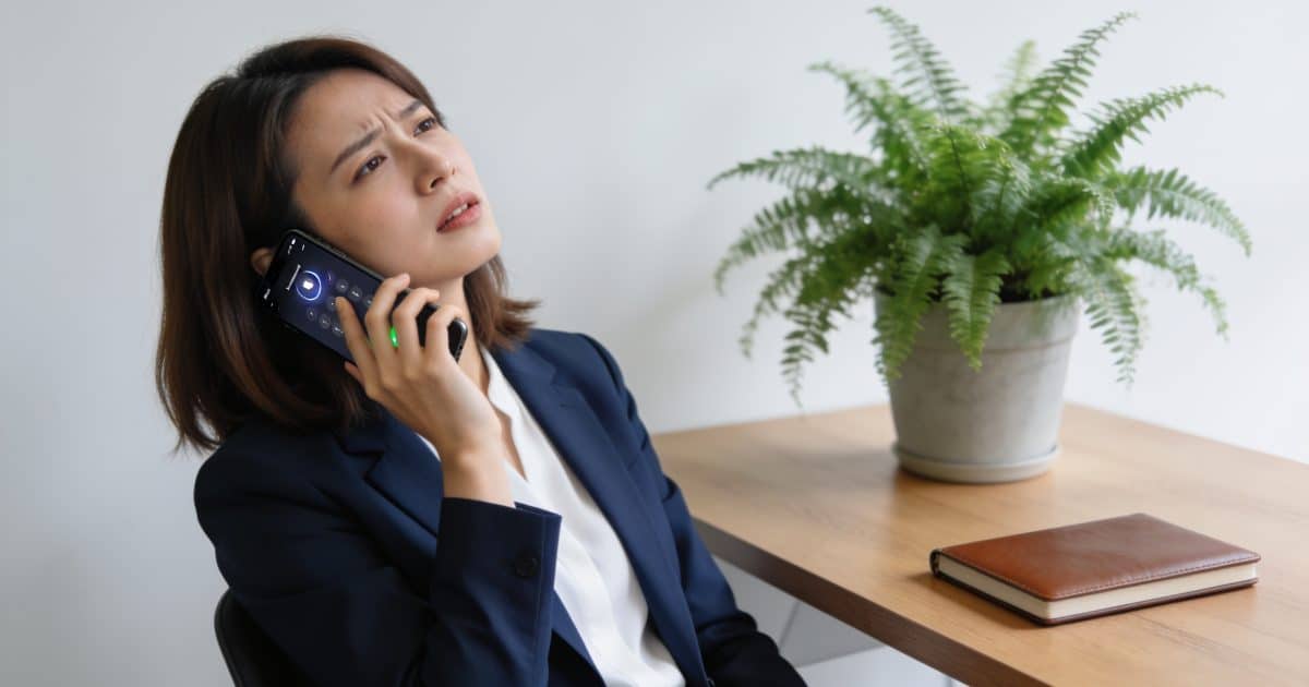 Femme agacée assise au bureau regardant smartphone sonnant